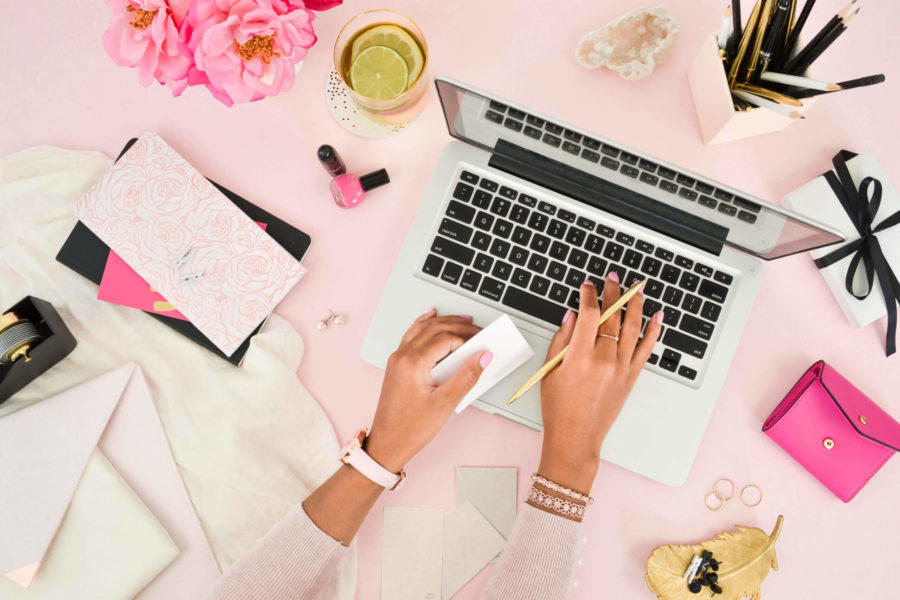 Image of someone typing on a laptop with a pink background and some accessories around the laptop