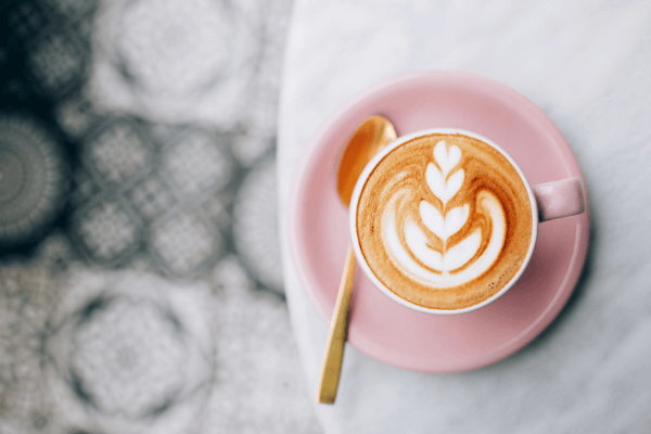 Pink cup of coffee with latte art and a golden spoon. Tiles display in the background.