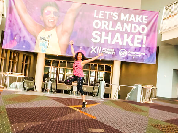 Diana jumping in front of the Let's Make Orlando Shake Zumba Convention banner in front of the Fitness Concert location