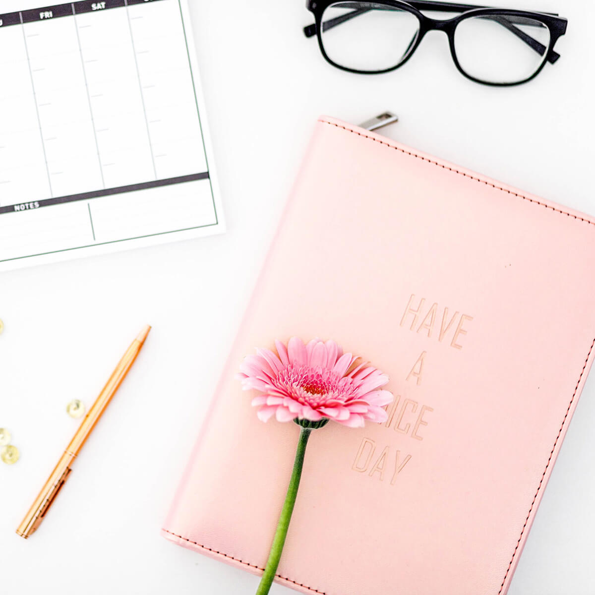 Flatlay with a notebook, flower, pen, glasses, and a planner