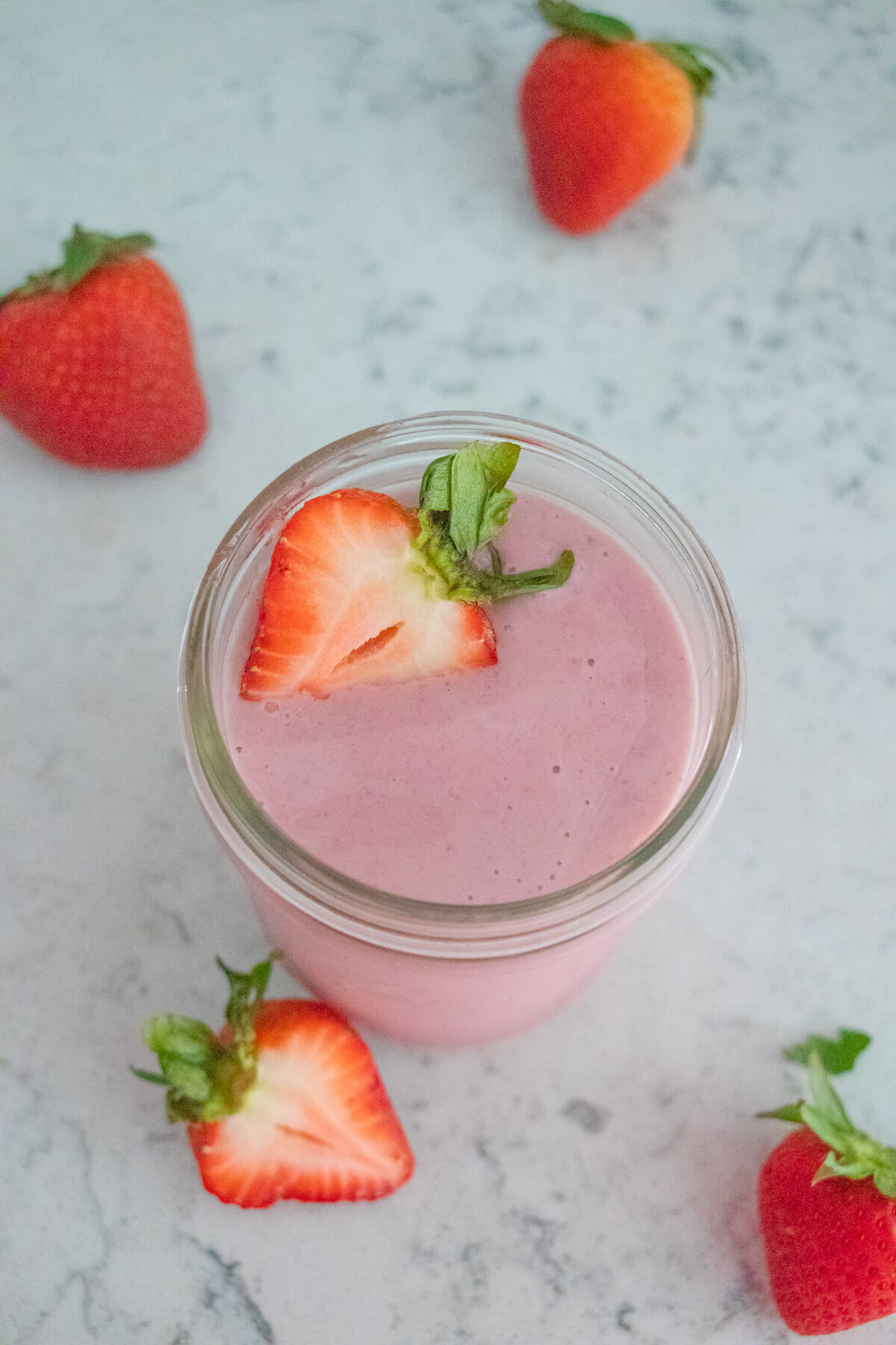 A top down shot of a strawberry smoothie with strawberries in the background