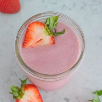 A top down shot of a strawberry smoothie with strawberries in the background