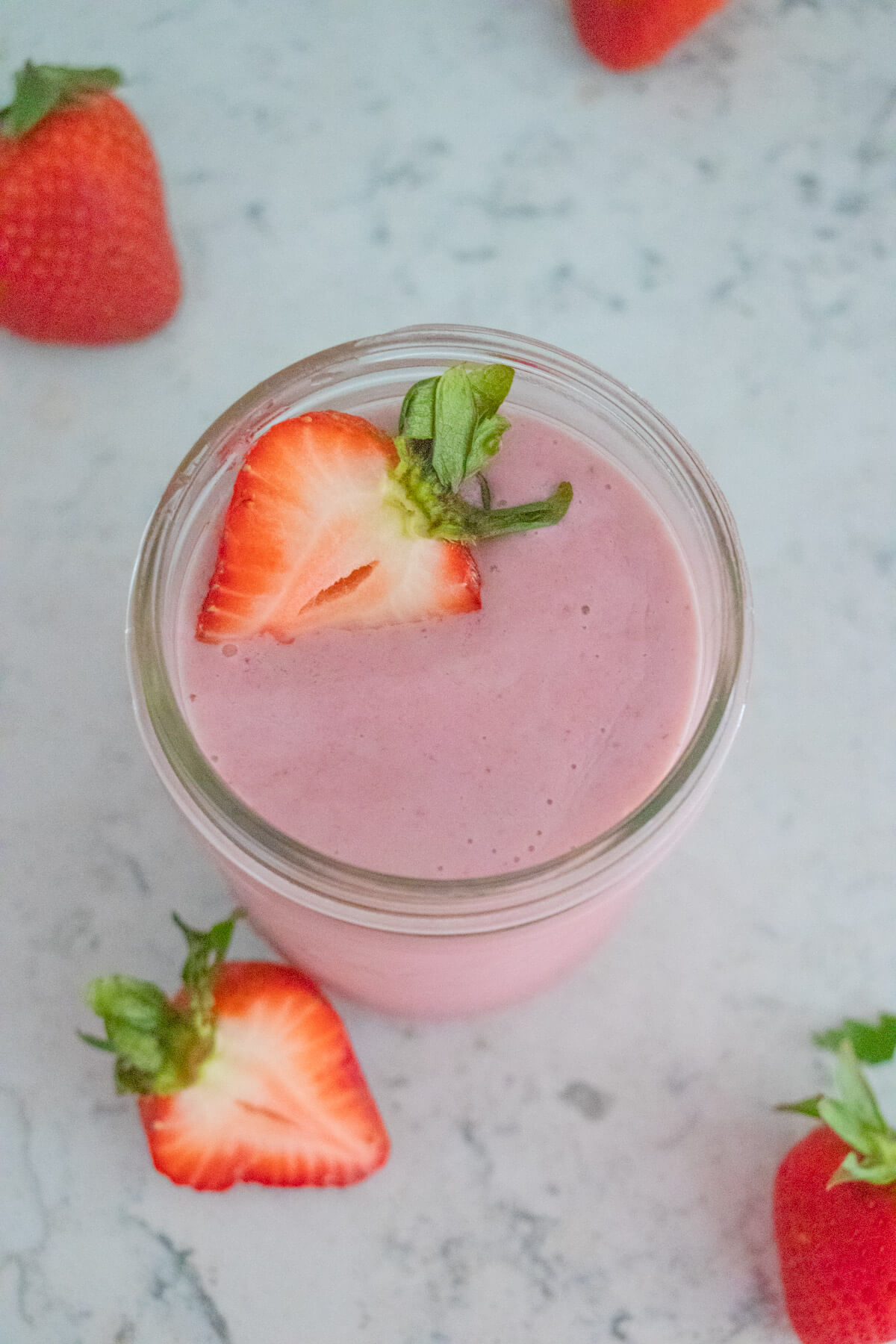 A top down shot of a strawberry smoothie with strawberries in the background